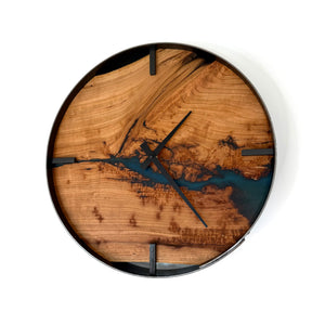 A round wall clock with a natural cherry wood grain face featuring a metallic teal resin river design, black hands, and a black outer rim, shown against a plain white background.